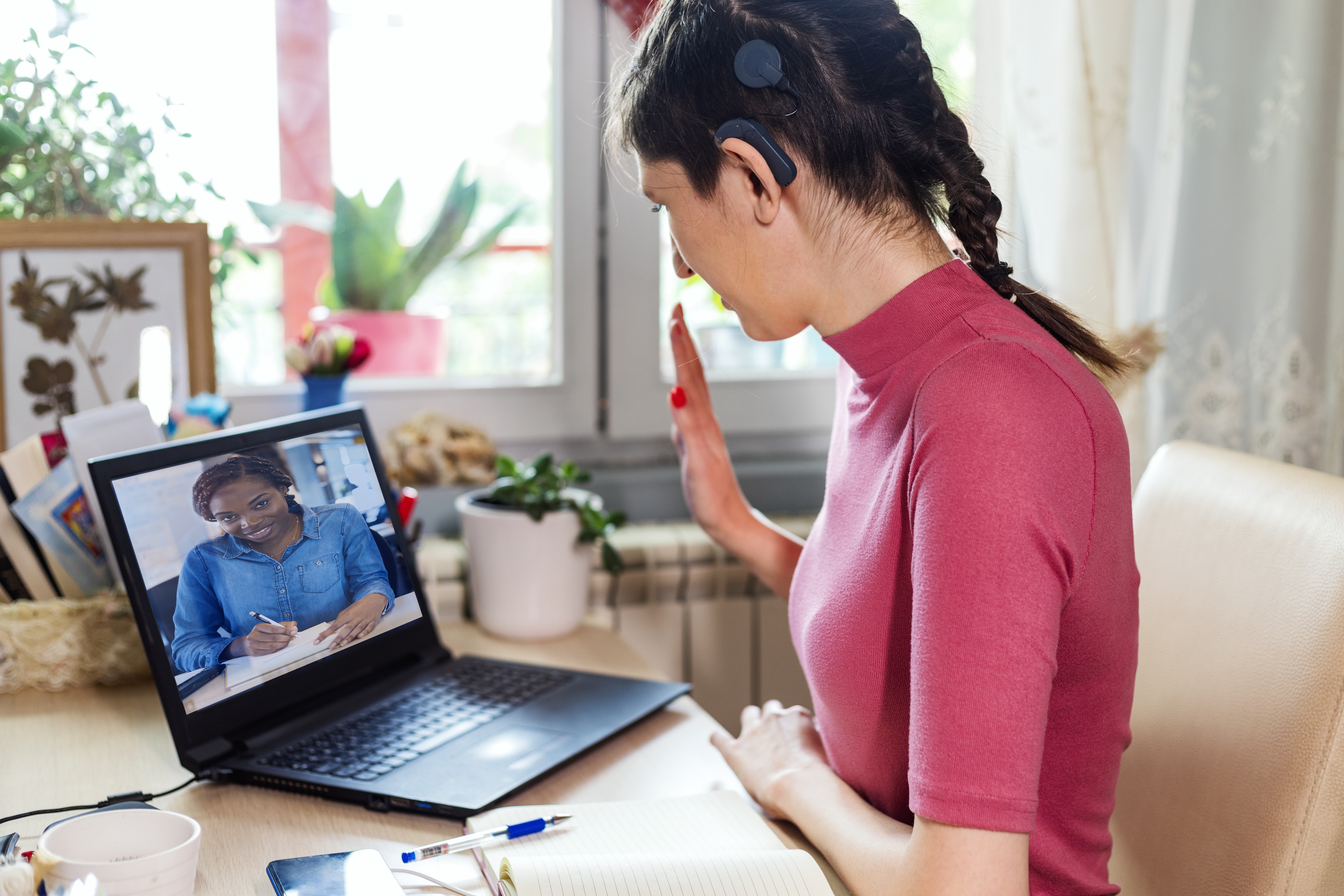 Young woman with cochlear implant studying online at home. She using modern technology.