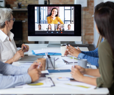 Hybrid meeting with people around a conference table looking at a screen with remote participants. Image by freepik.