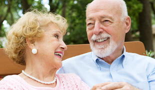 Happy senior couple laughing together.  She is wearing a hearing aid.